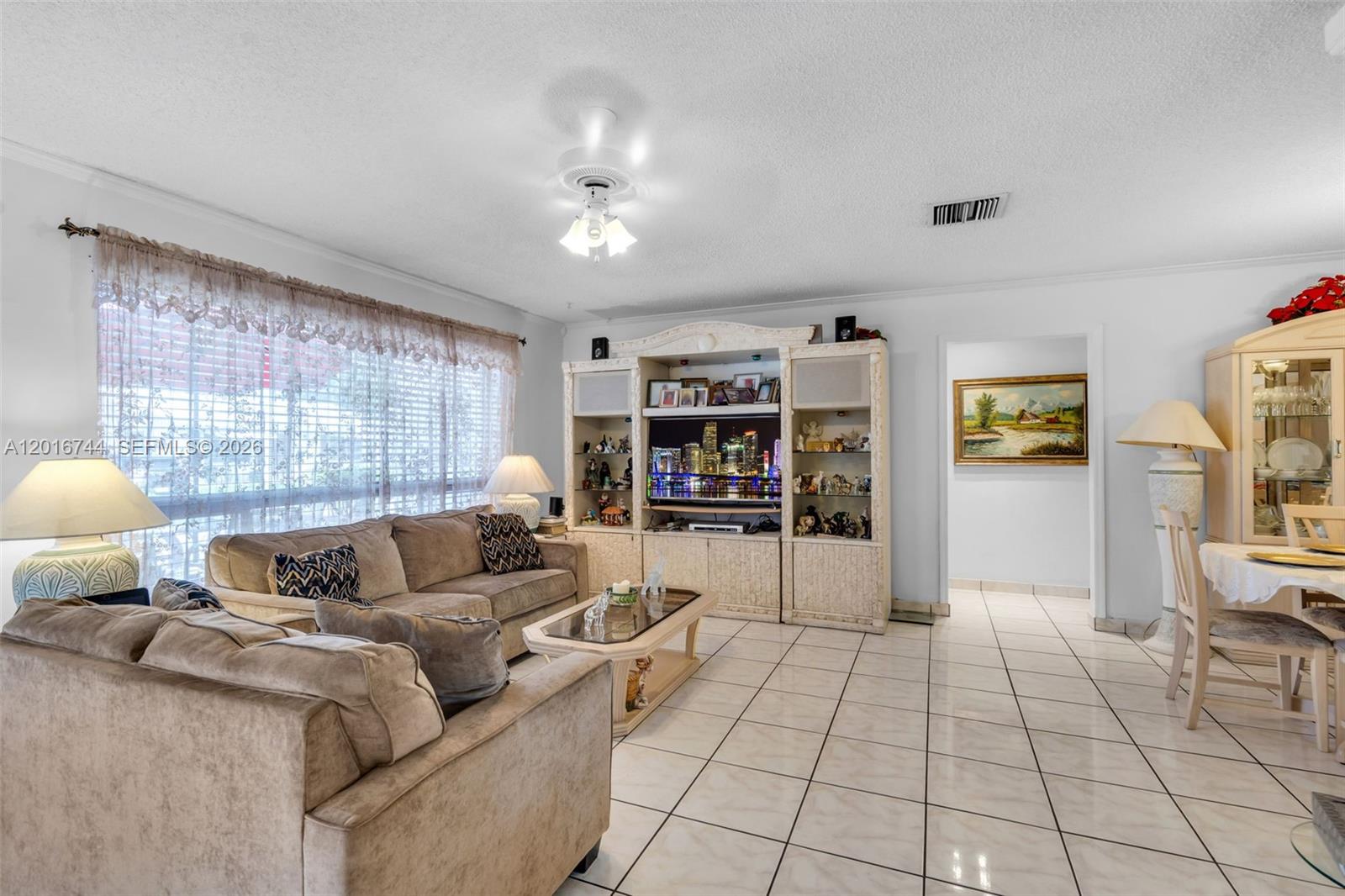 A living room with tile floors, a beige sofa, and a large entertainment center — 5809 NW 83rd Ave, Tamarac FL 33321, TAMARAC, FL