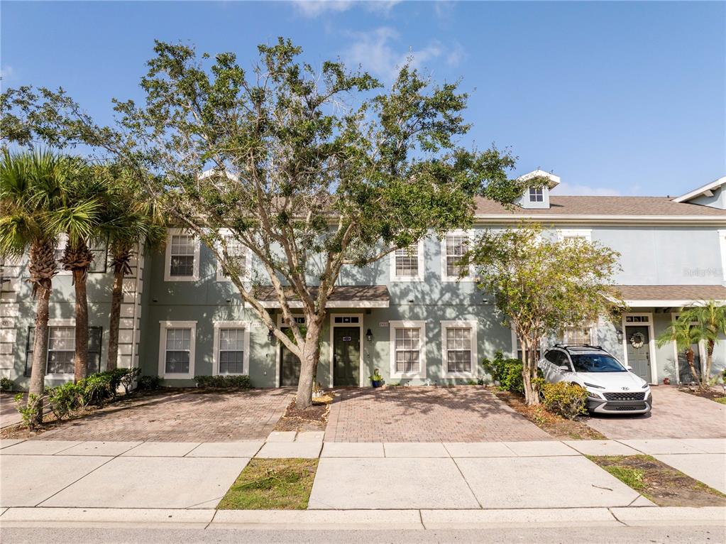 A two-story townhouse exterior features a paved driveway, a large tree, and a white SUV — 2433 CARAVELLE CIRCLE, KISSIMMEE, FL