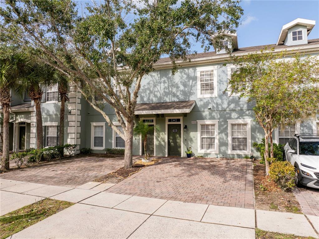 A two-story townhouse with a light green exterior, brick driveway, and a white car parked — 2433 CARAVELLE CIRCLE, KISSIMMEE, FL