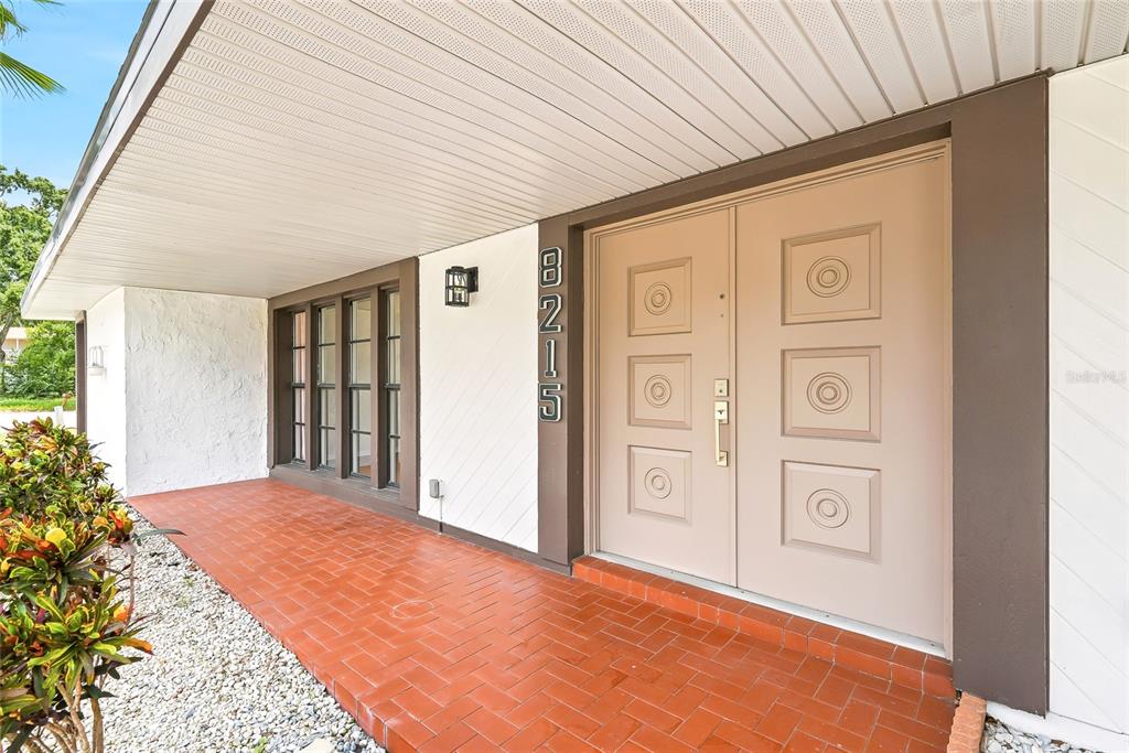 A covered porch with red brick flooring leads to a double door entrance — 8215 LA SERENA DRIVE, TAMPA, FL