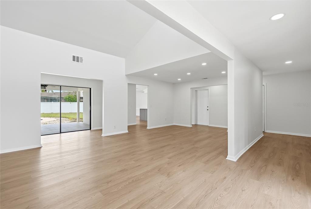 A bright, open-concept living area features light wood-look flooring, recessed lighting, and a vaulted ceiling — 8215 LA SERENA DRIVE, TAMPA, FL