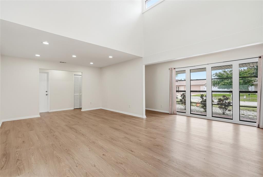 An empty living room features light wood-look flooring, recessed lighting, and a large glass door — 8215 LA SERENA DRIVE, TAMPA, FL