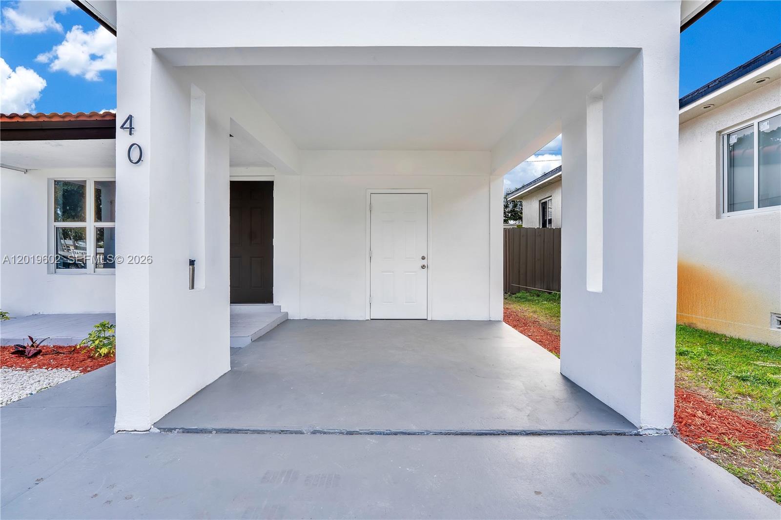 A white carport with a gray concrete floor features a dark door and a white door — 40 SE 3RD TERR, Dania Beach FL 33004, DANIA BEACH, FL
