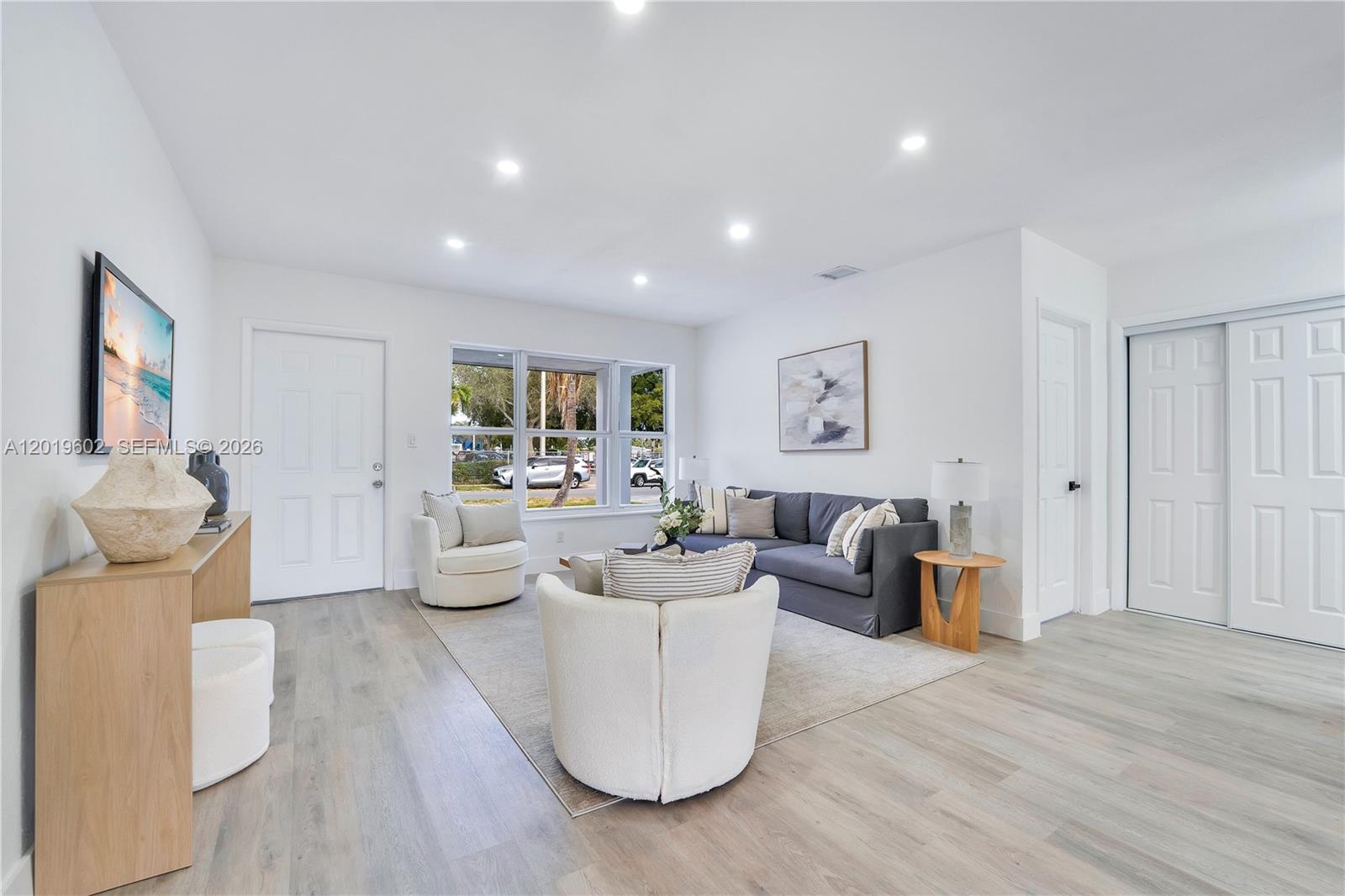 A living room features a grey sofa, two white armchairs, and light wood-look flooring — 40 SE 3RD TERR, Dania Beach FL 33004, DANIA BEACH, FL