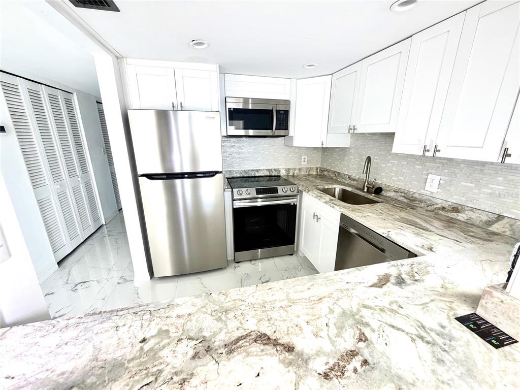 A kitchen features white cabinets, stainless steel appliances, and a marble-patterned countertop — 4550 COVE CIRCLE UNIT 905, ST PETERSBURG, FL