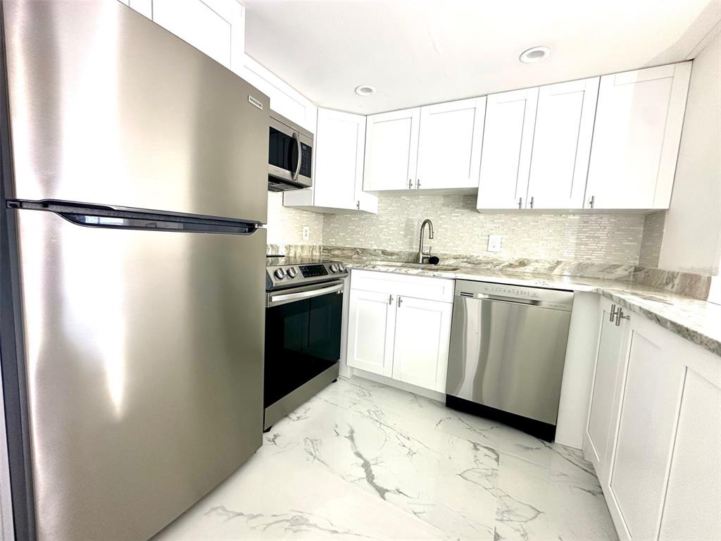 A kitchen features white cabinets, stainless steel appliances, marble-patterned flooring, and a tiled backsplash — 4550 COVE CIRCLE UNIT 905, ST PETERSBURG, FL