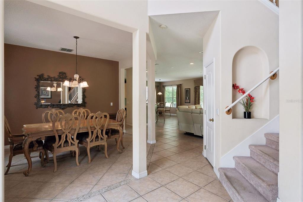 A dining room with a wooden table and chairs sits beside a staircase and hallway — 2582 DOUBLE TREE PLACE, OVIEDO, FL