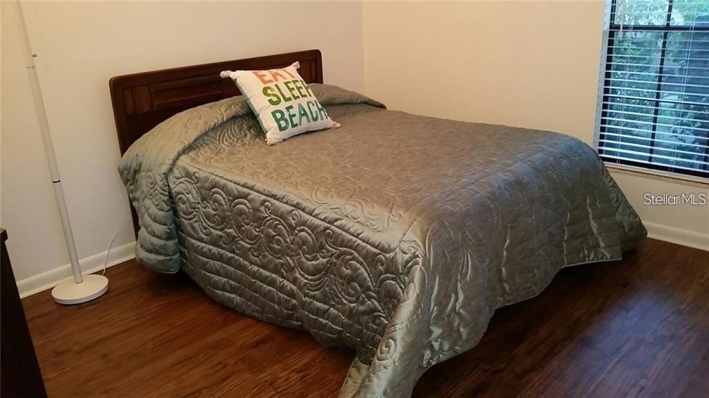 A bedroom features a wooden bed frame, a quilted gray bedspread, and wood-look flooring — 4581 MORNINGSIDE UNIT 21, SARASOTA, FL