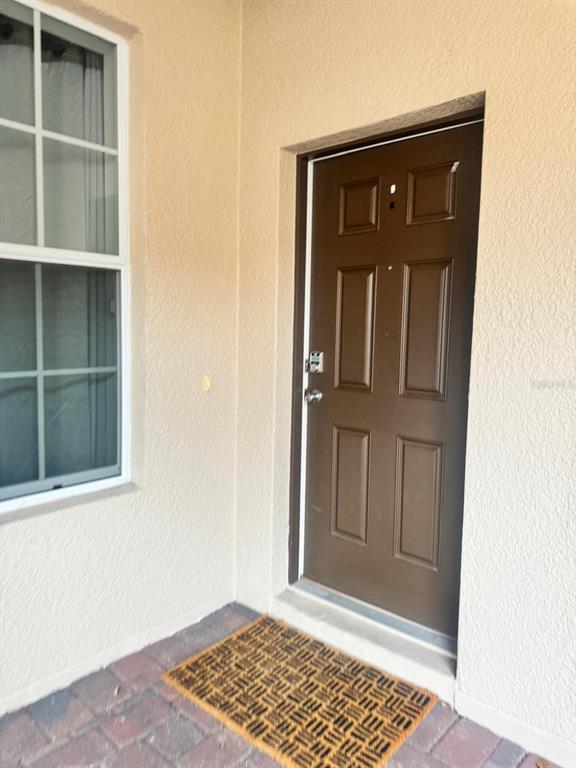 A brown front door with a keypad lock sits next to a window on a patio — 26715 BELLA VISTA DRIVE, HOWEY IN THE HILLS, FL