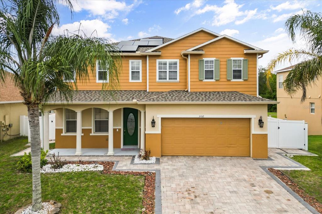 A two-story house with yellow siding, a two-car garage, and solar panels on the roof — 3332 WHISTLING TRAIL, ST CLOUD, FL