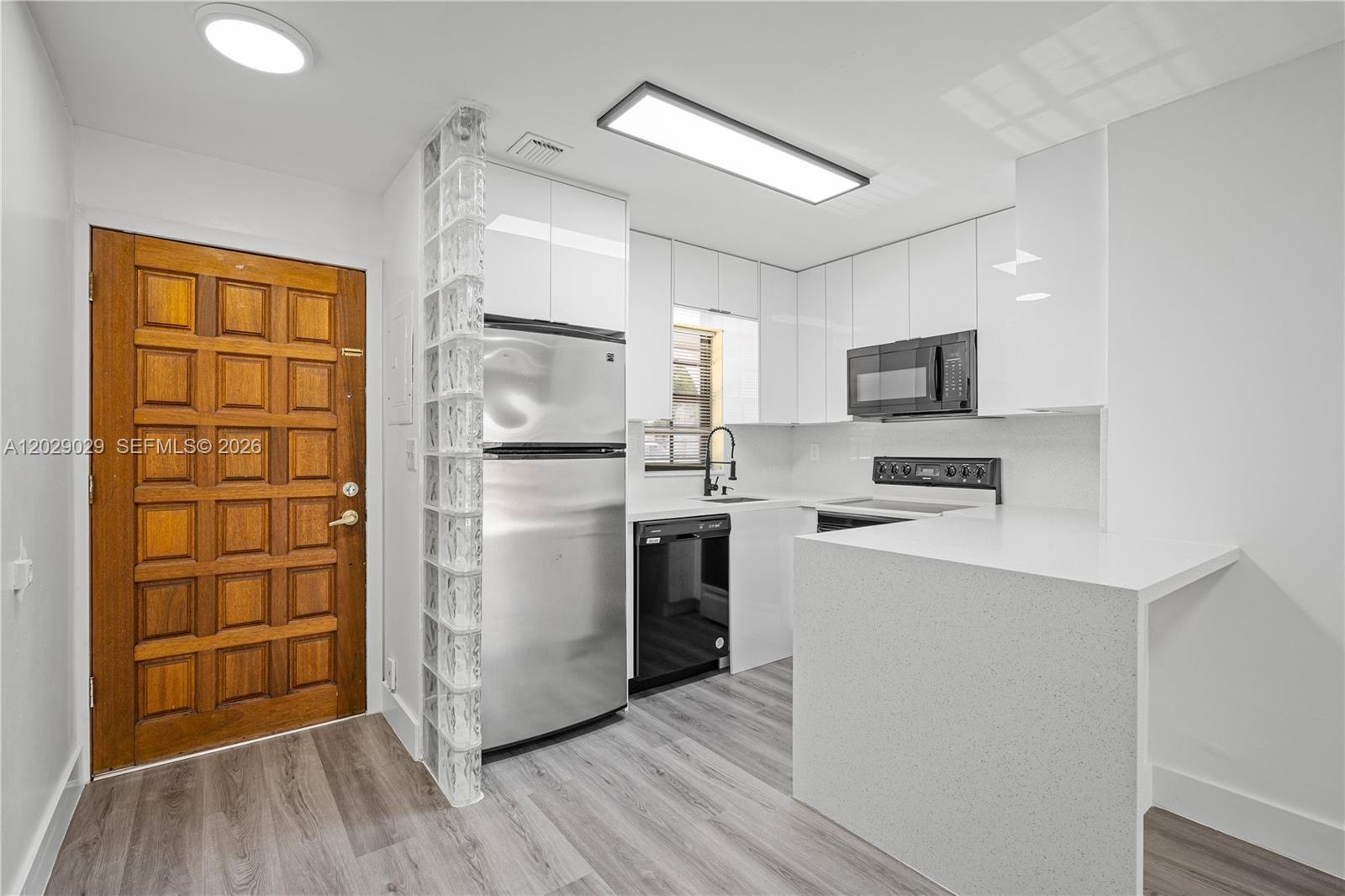 A modern kitchen features white cabinetry, stainless steel appliances, and a glass block partition wall — 12035 SW 18th St # 48, Miami FL 33175, MIAMI, FL