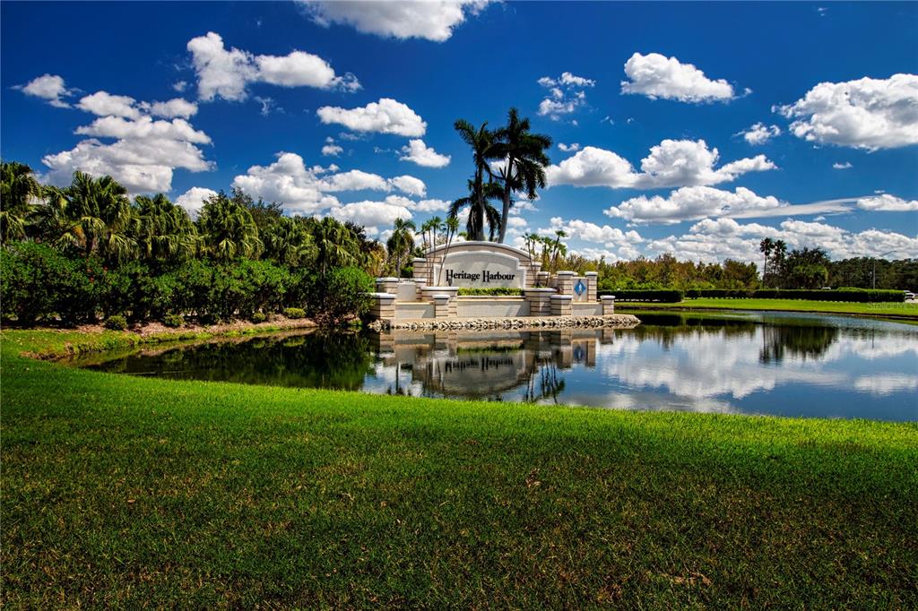 A stone monument sign for Heritage Harbour sits behind a pond surrounded by palm trees — 267 HERITAGE ISLES WAY, BRADENTON, FL