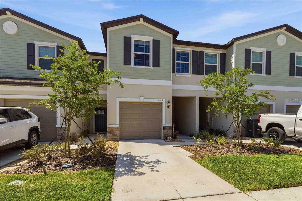 A two-story townhouse exterior with a single-car garage, light green siding, and a concrete driveway — 2549 SUNRAY VENUS WAY, RUSKIN, FL