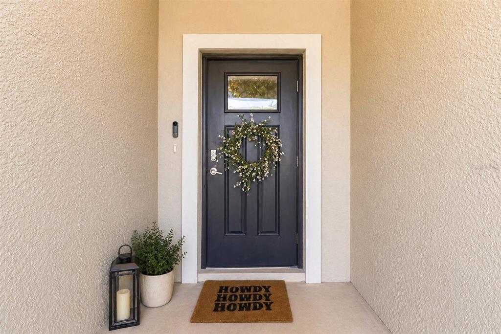 A dark front door with a wreath and a doormat sits in a stucco entryway — 2549 SUNRAY VENUS WAY, RUSKIN, FL