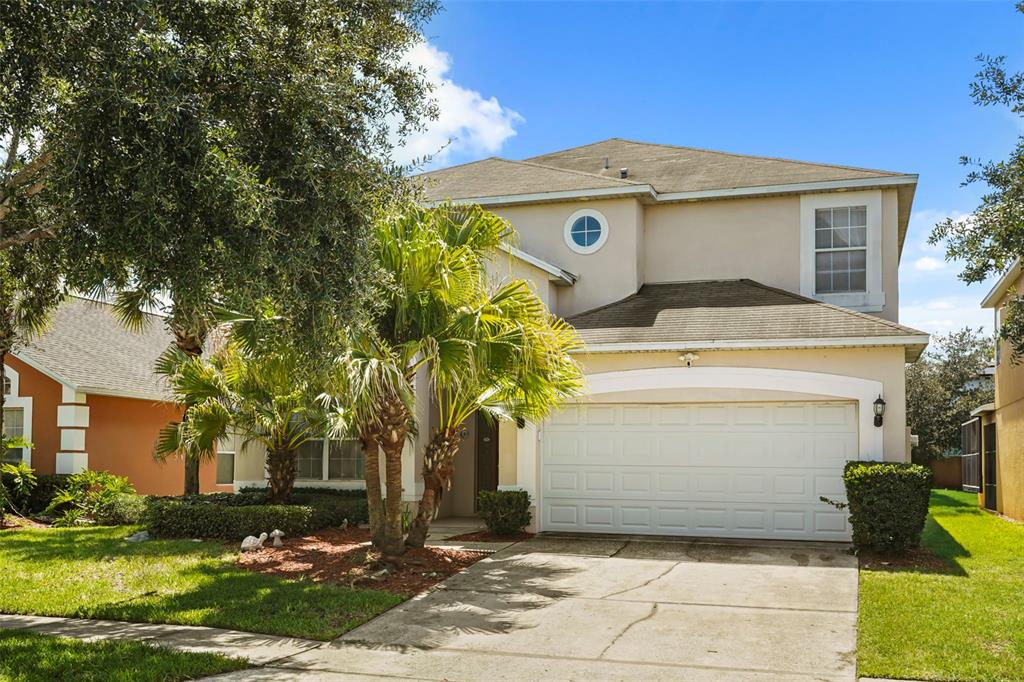 A two-story suburban house with a beige stucco exterior, a two-car garage, and palm trees — 1265 SEASONS BOULEVARD, KISSIMMEE, FL