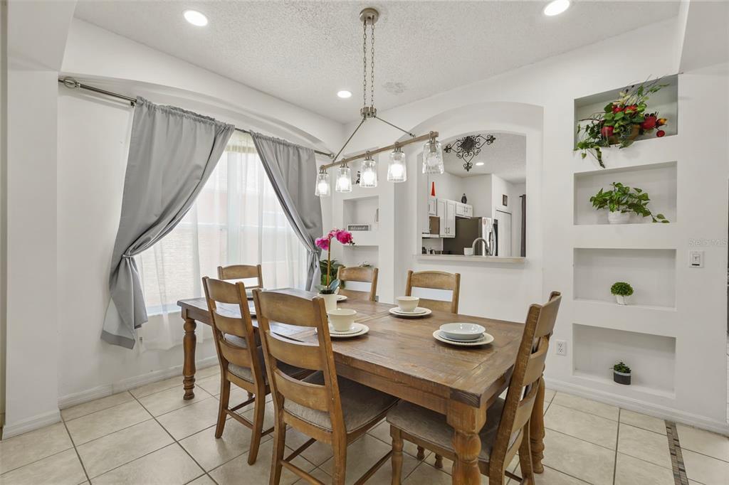 A dining room features a wooden table, chairs, tile flooring, and built-in wall niches — 1265 SEASONS BOULEVARD, KISSIMMEE, FL