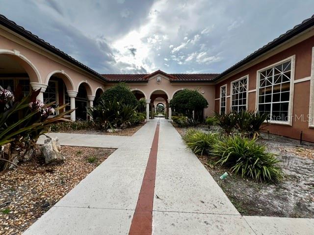 A paved walkway leads toward the arched entrance of a tan building under a cloudy sky — 2701 ORLANDO WEST DRIVE, ORLANDO, FL