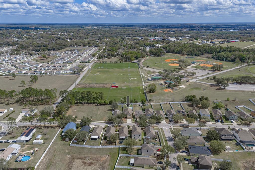 An aerial view shows a residential neighborhood adjacent to a large park with sports fields — 13416 KENT BRADLEY STREET, DADE CITY, FL