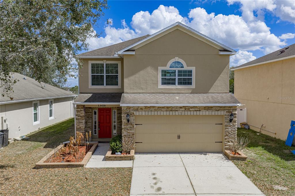 A two-story house with a tan stucco exterior, stone accents, and a red front door — 13416 KENT BRADLEY STREET, DADE CITY, FL
