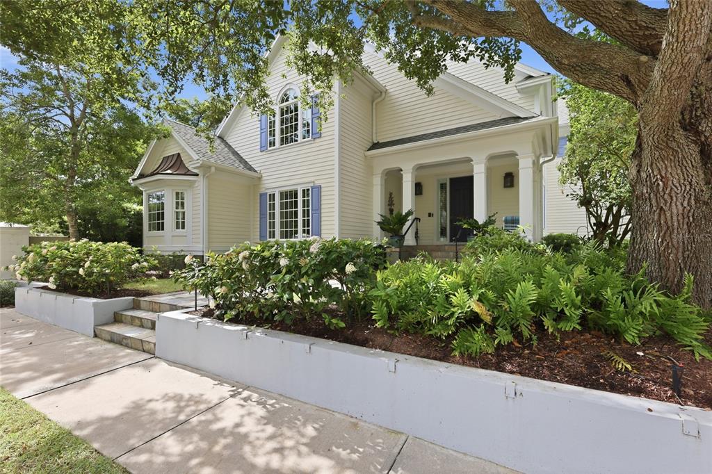 A two-story light yellow house with blue shutters features a front porch and retaining wall — 1798 LINCOLN PARK CIRCLE, SARASOTA, FL