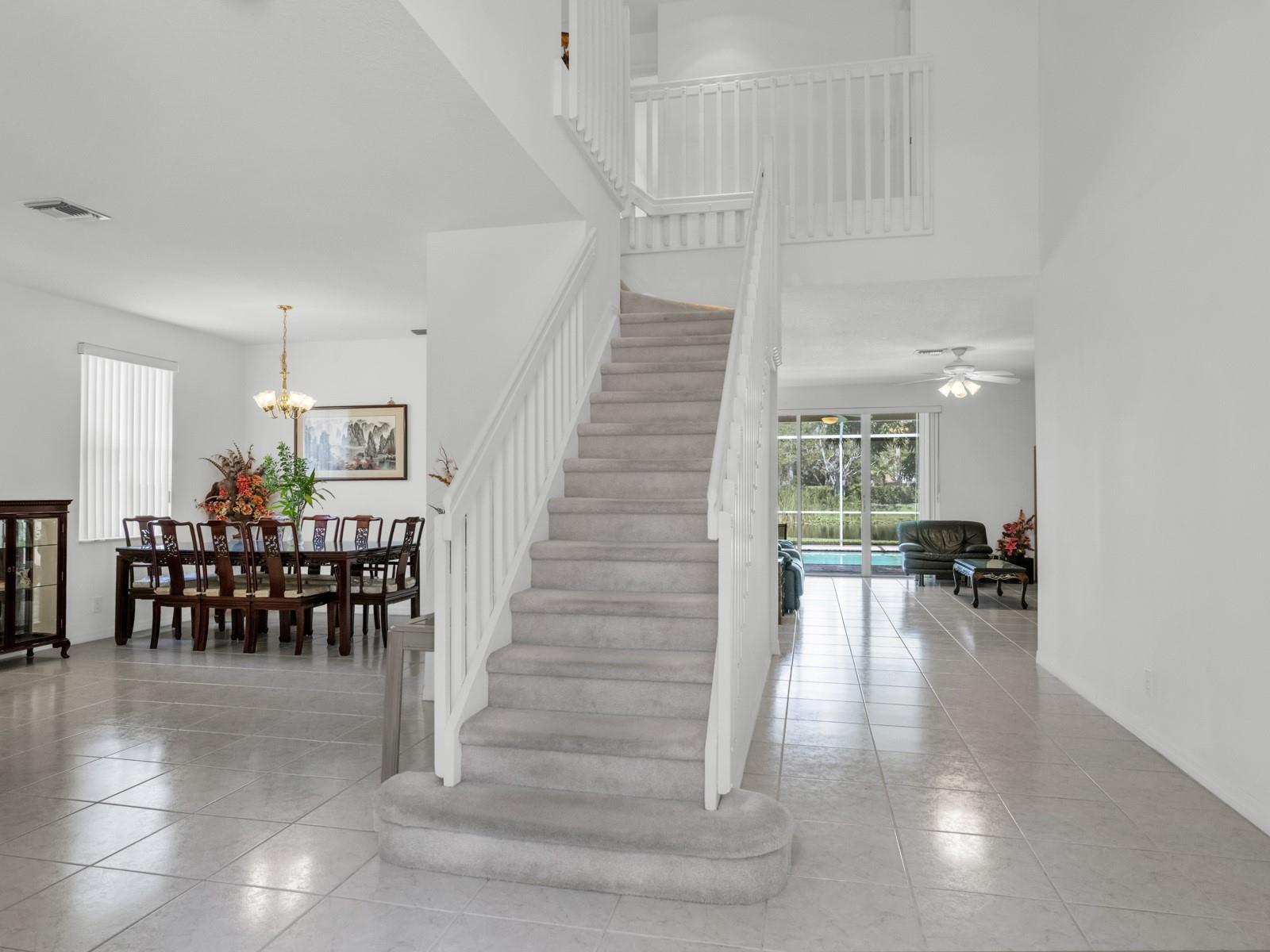 A carpeted staircase with white railings sits in the center of a tiled foyer — 4032 Pinewood Lane, Weston FL 33331, WESTON, FL
