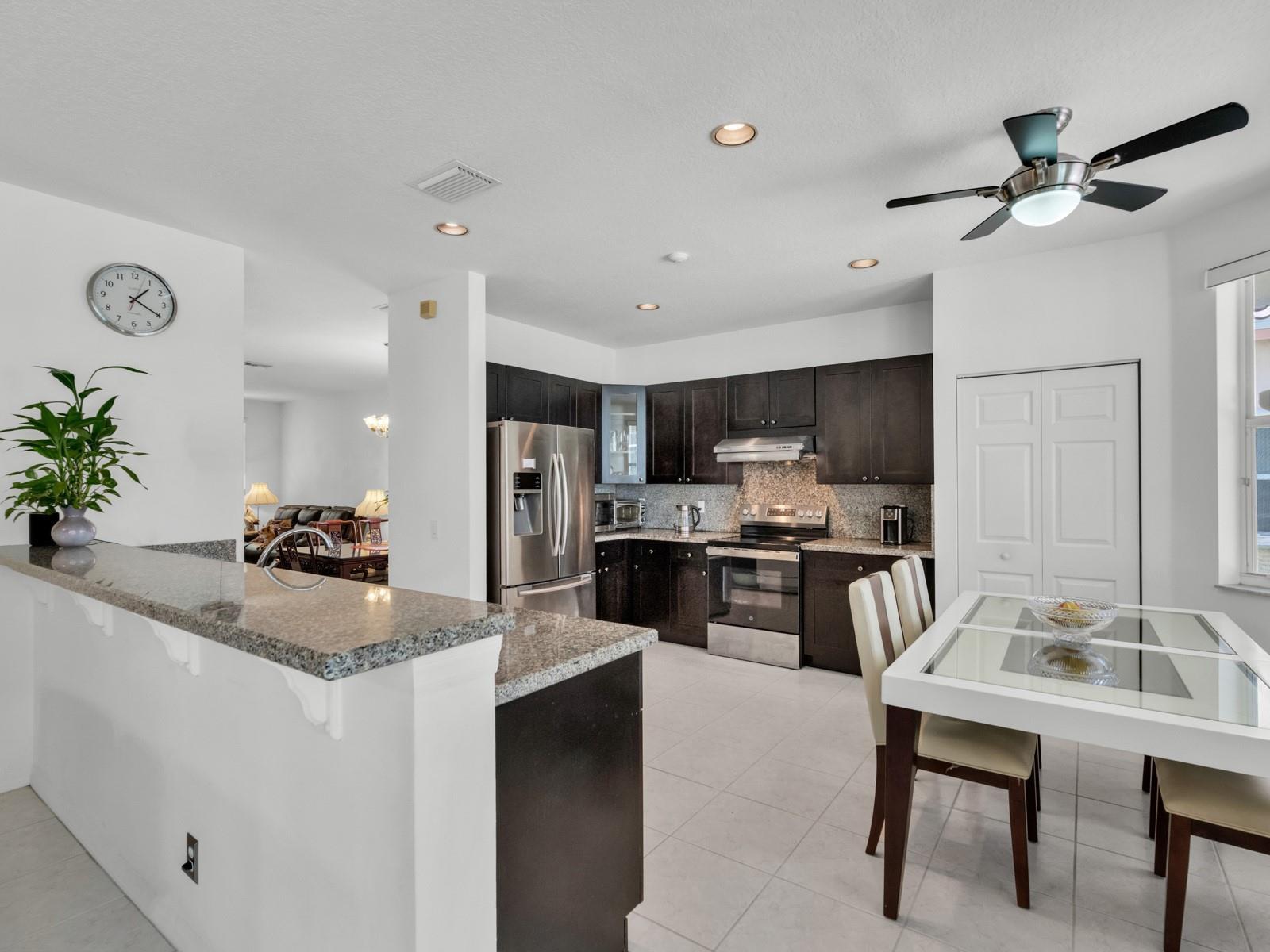 A kitchen with dark wood cabinets, granite countertops, stainless steel appliances, and a dining area — 4032 Pinewood Lane, Weston FL 33331, WESTON, FL