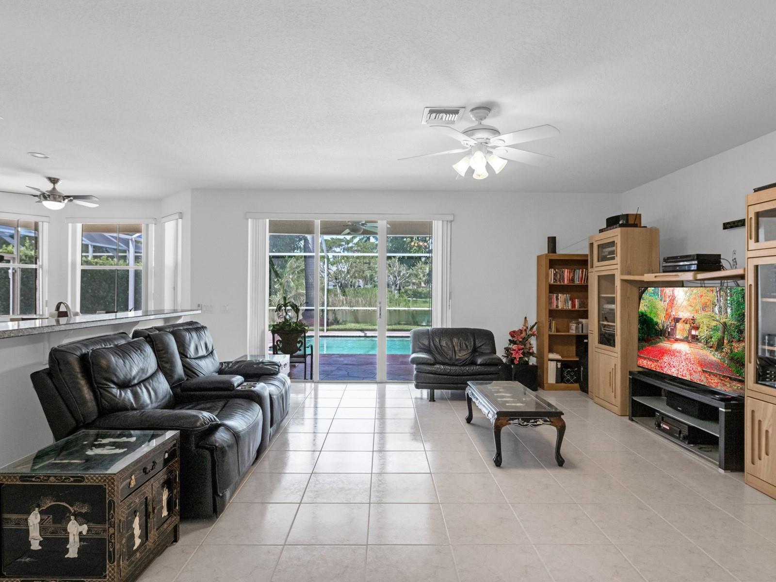 A living room with tile floors, black leather furniture, a media center, and pool views — 4032 Pinewood Lane, Weston FL 33331, WESTON, FL