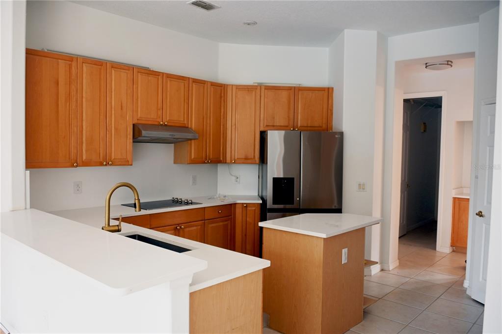 A kitchen features wood cabinets, white countertops, a stainless steel refrigerator, and a small island — 8800 OAK LANDINGS COURT, ORLANDO, FL
