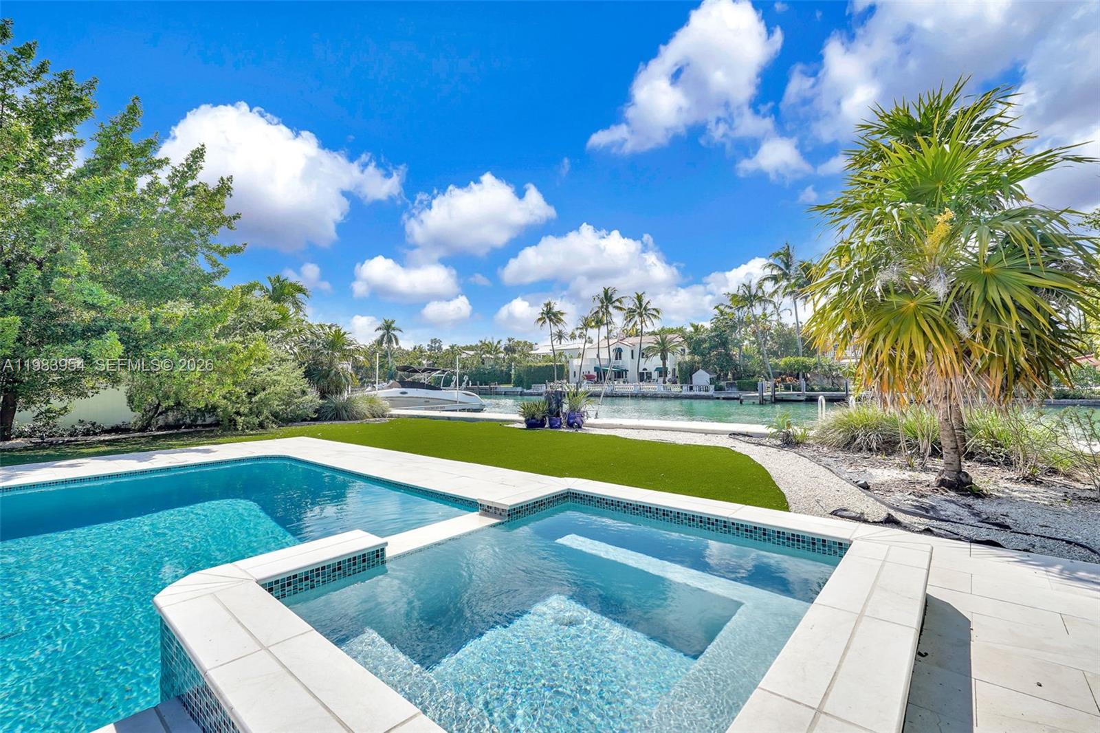 A swimming pool and spa overlook a canal with a boat and palm trees — 4560 Prairie Ave, Miami Beach FL 33140, MIAMI BEACH, FL