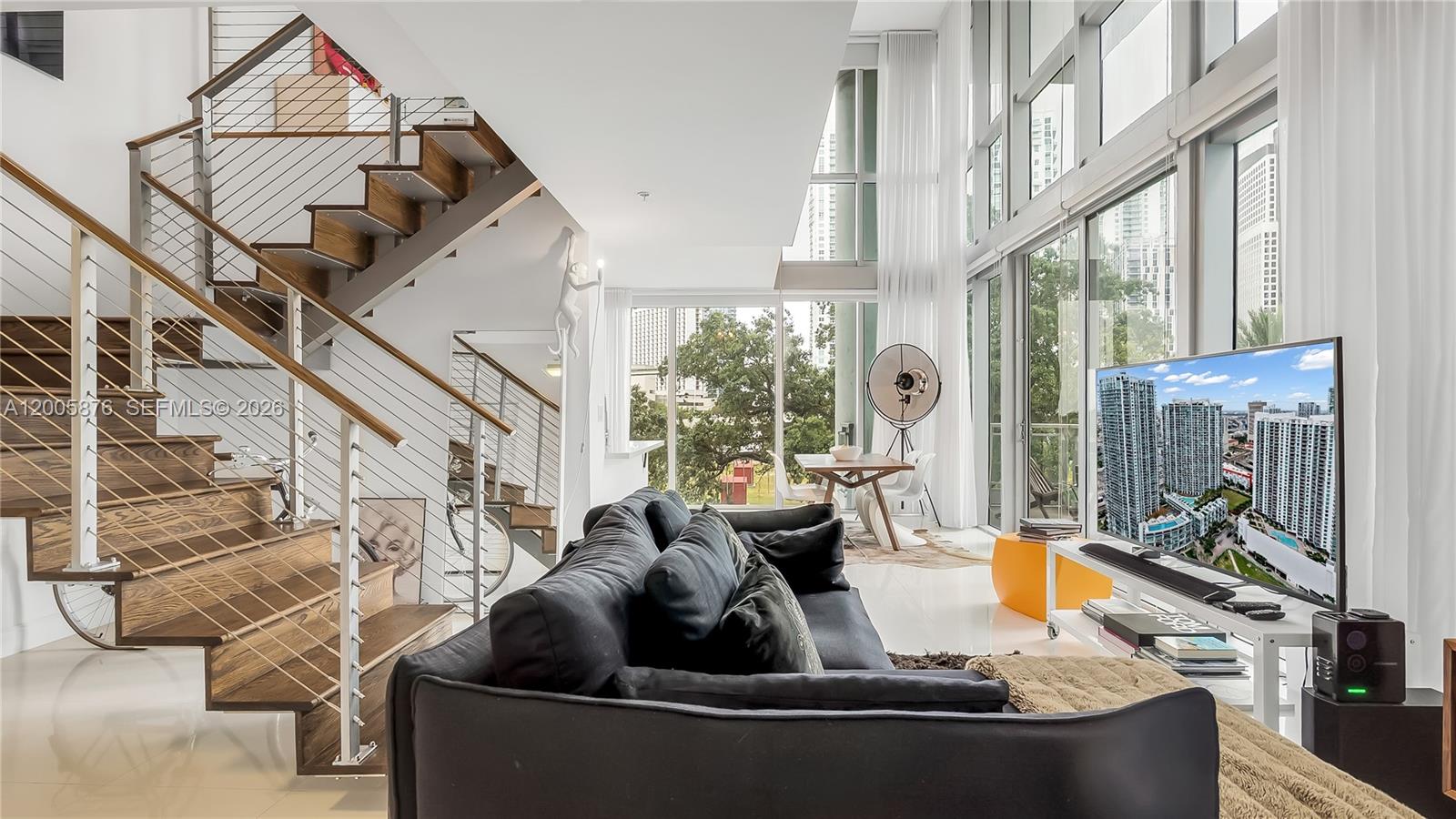 A modern living room features a wooden staircase, a dark sofa, and floor-to-ceiling windows — 90 SW 3rd St # 308, Miami FL 33130, MIAMI, FL