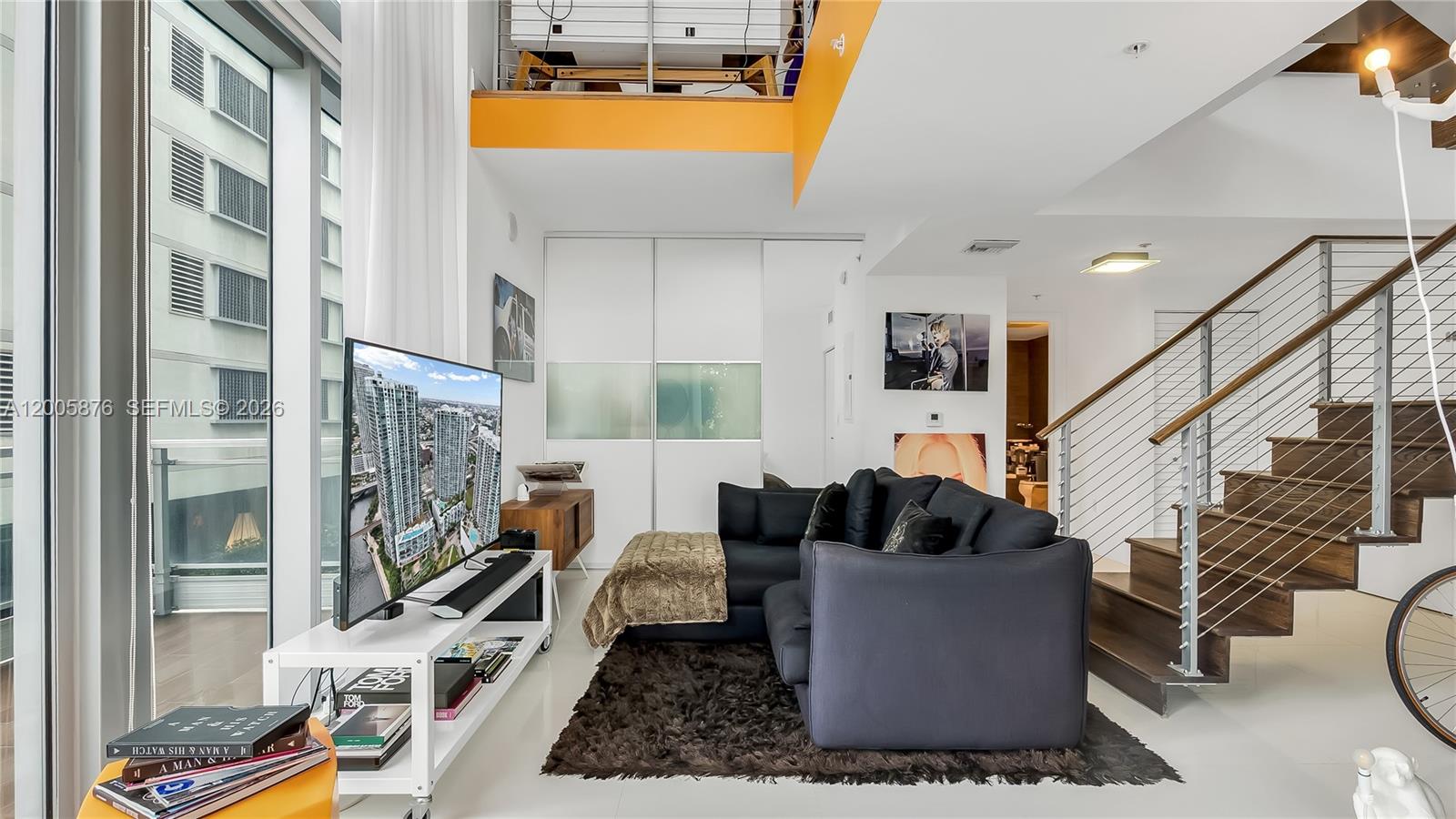 A living room features a dark sectional sofa, a television, and a wooden staircase — 90 SW 3rd St # 308, Miami FL 33130, MIAMI, FL