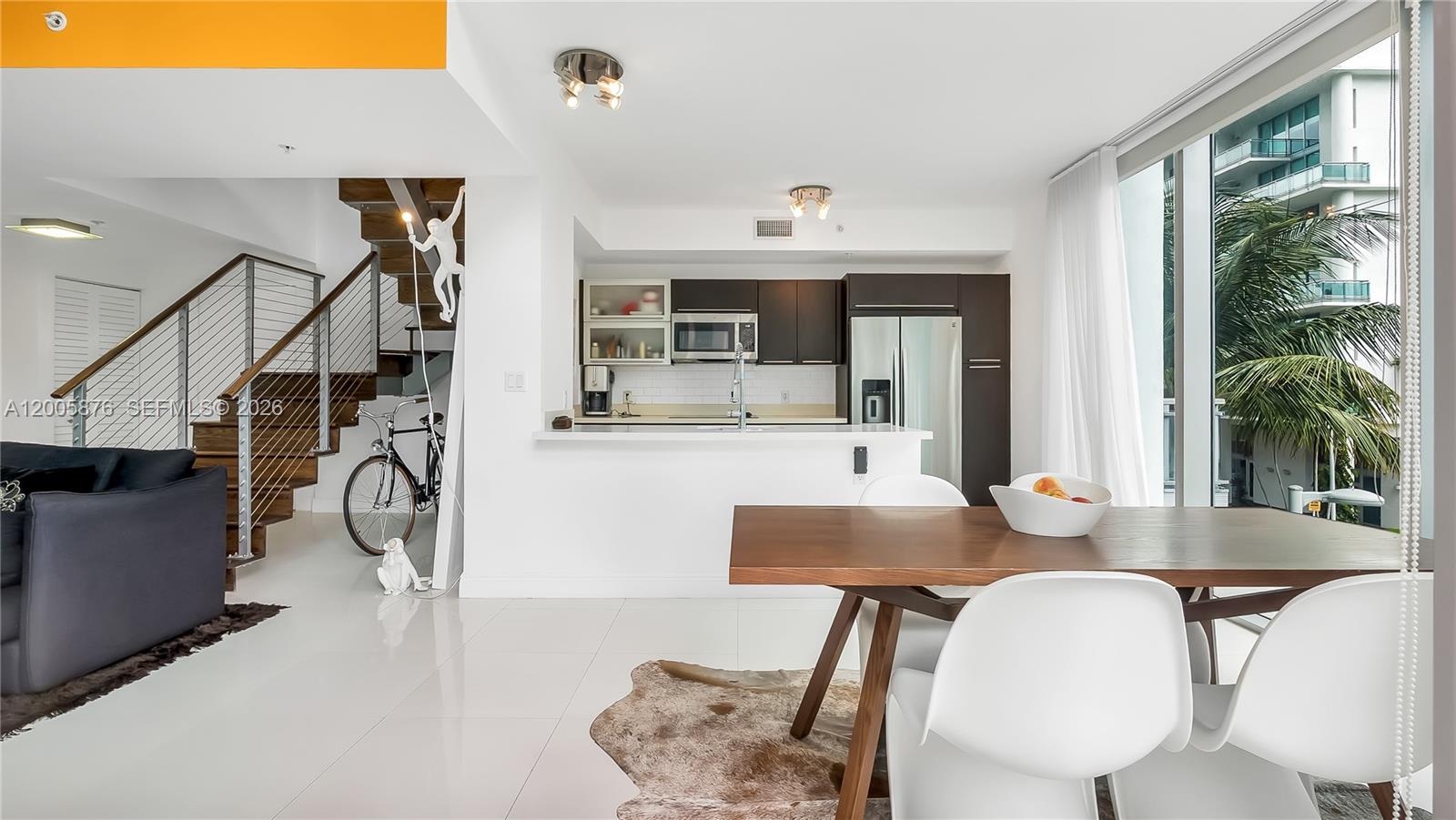 A modern kitchen and dining area feature white tile floors, a wooden staircase, and balcony views — 90 SW 3rd St # 308, Miami FL 33130, MIAMI, FL