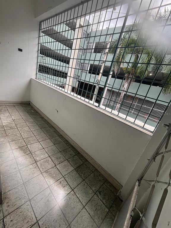 A tiled balcony with a metal security grate overlooks a multi-story parking garage and palm tree — 26 MANUEL CORCHADO UNIT ! A, AGUADILLA, PR