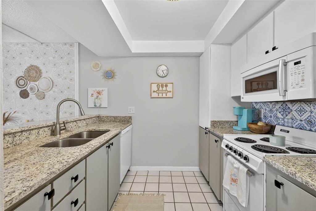 A kitchen features granite countertops, white cabinets, a stainless steel sink, and a tiled floor — 2614 COVE CAY DRIVE UNIT 405, CLEARWATER, FL