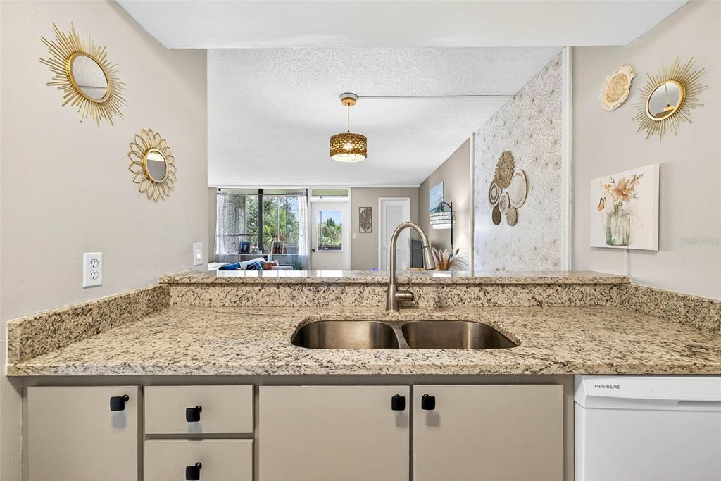 A kitchen sink with granite countertops overlooks a living area with decorative wall mirrors — 2614 COVE CAY DRIVE UNIT 405, CLEARWATER, FL
