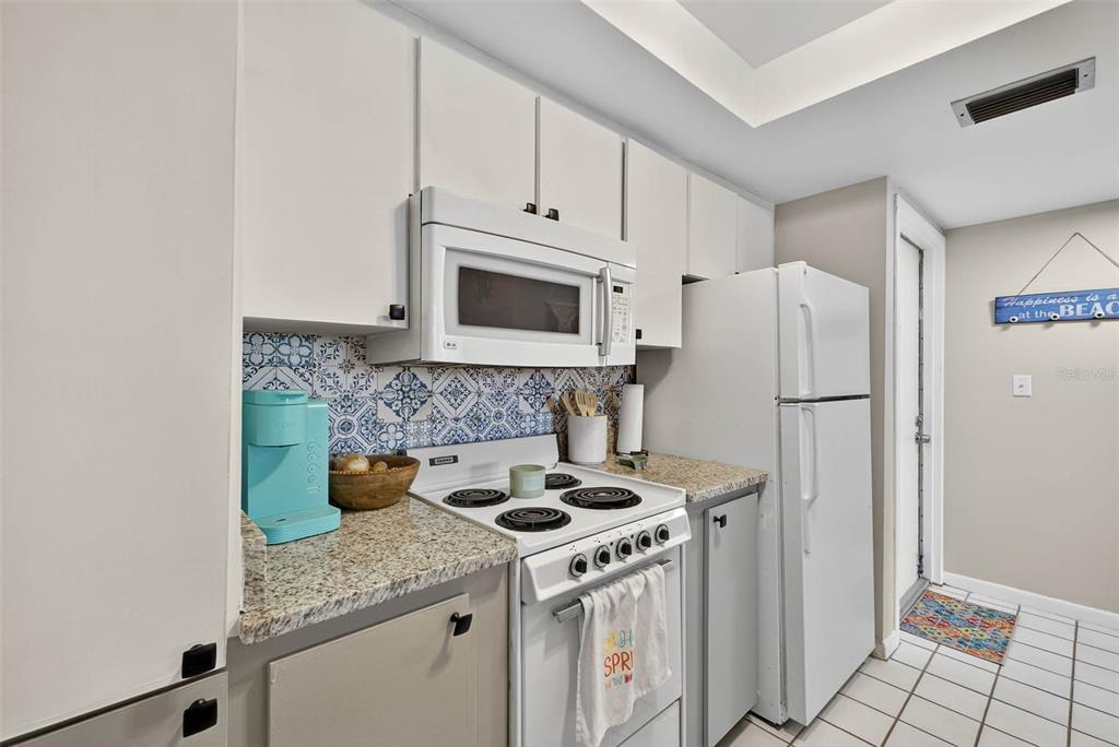 A kitchen features white cabinets, a white microwave, a white stove, and blue patterned backsplash — 2614 COVE CAY DRIVE UNIT 405, CLEARWATER, FL