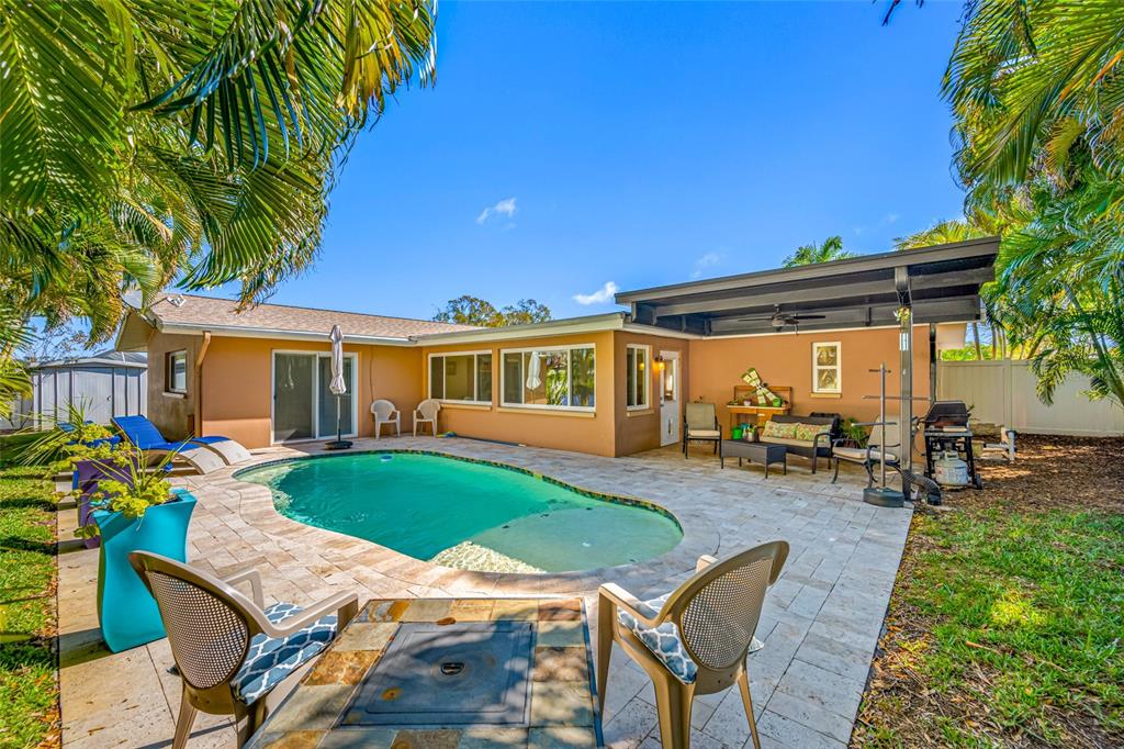 A backyard features a swimming pool, a stone patio, and a covered seating area — 12957 90TH TERRACE, SEMINOLE, FL