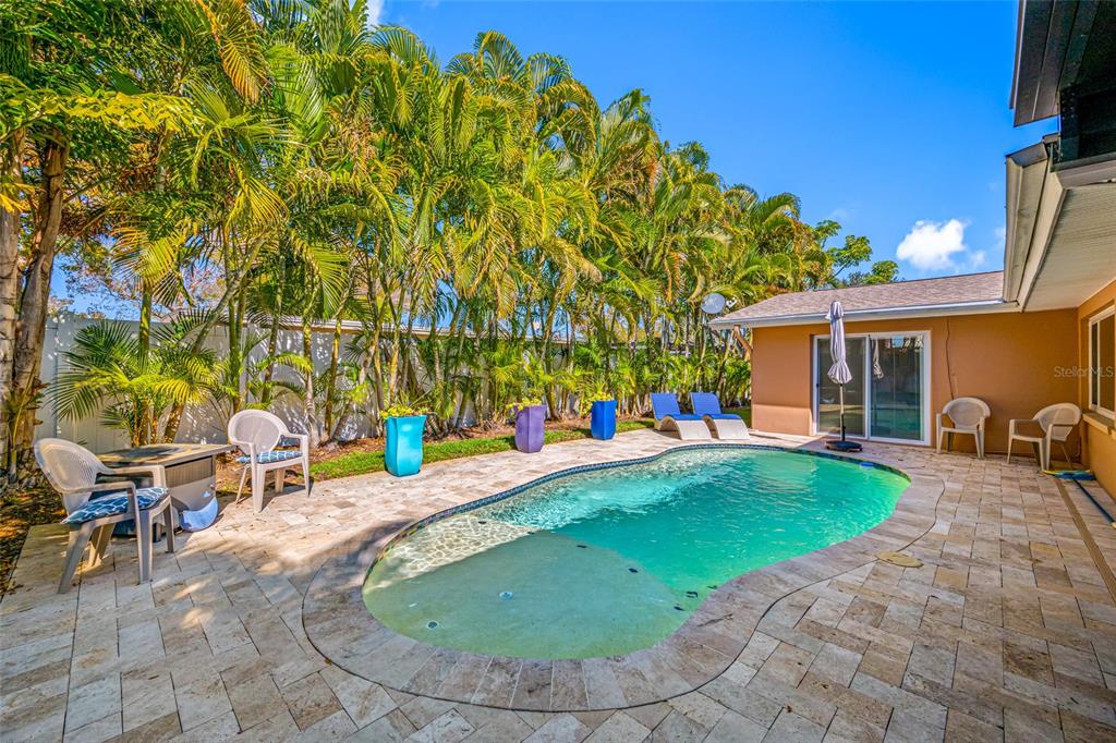 A backyard features a kidney-shaped swimming pool surrounded by a stone patio and palm trees — 12957 90TH TERRACE, SEMINOLE, FL