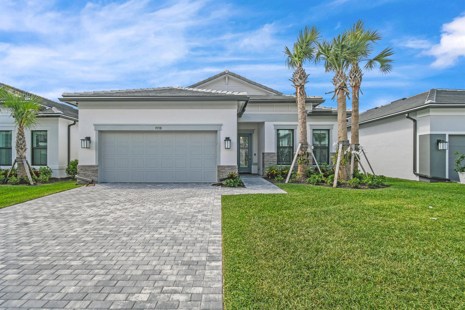 A single-story house with a gray garage, paved driveway, and palm trees in the front yard — 9358 Cape Honey Bee Lane, Lake Worth FL 33467, LAKE WORTH, FL