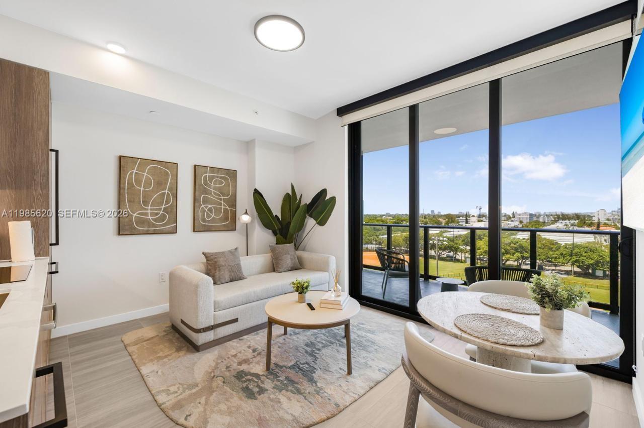 A modern living room with a sofa, dining area, and balcony overlooking a park — 580 72nd St # 613, Miami Beach FL 33141, MIAMI BEACH, FL