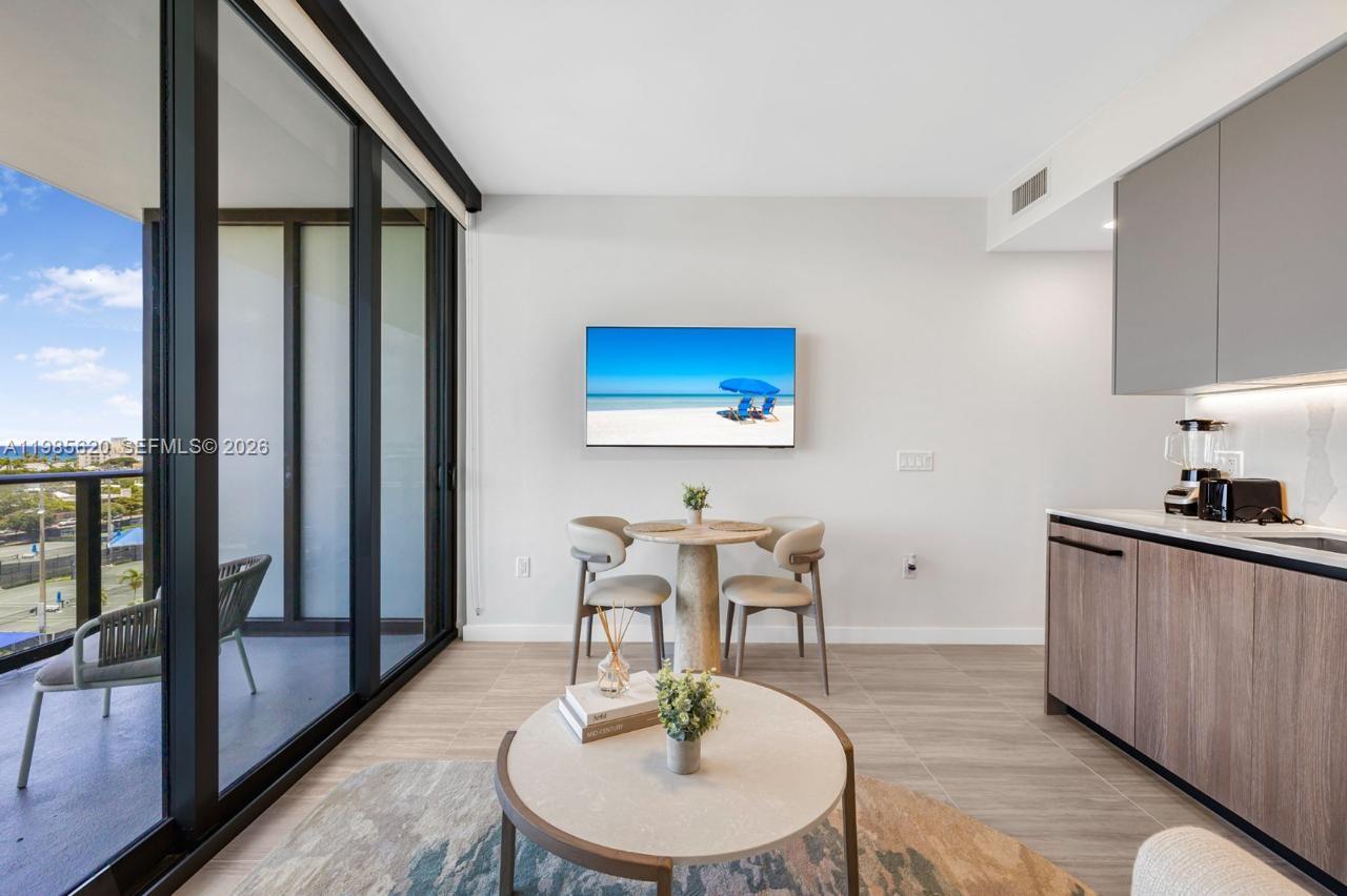 A modern apartment living area features a dining set, wall-mounted television, and balcony access — 580 72nd St # 613, Miami Beach FL 33141, MIAMI BEACH, FL
