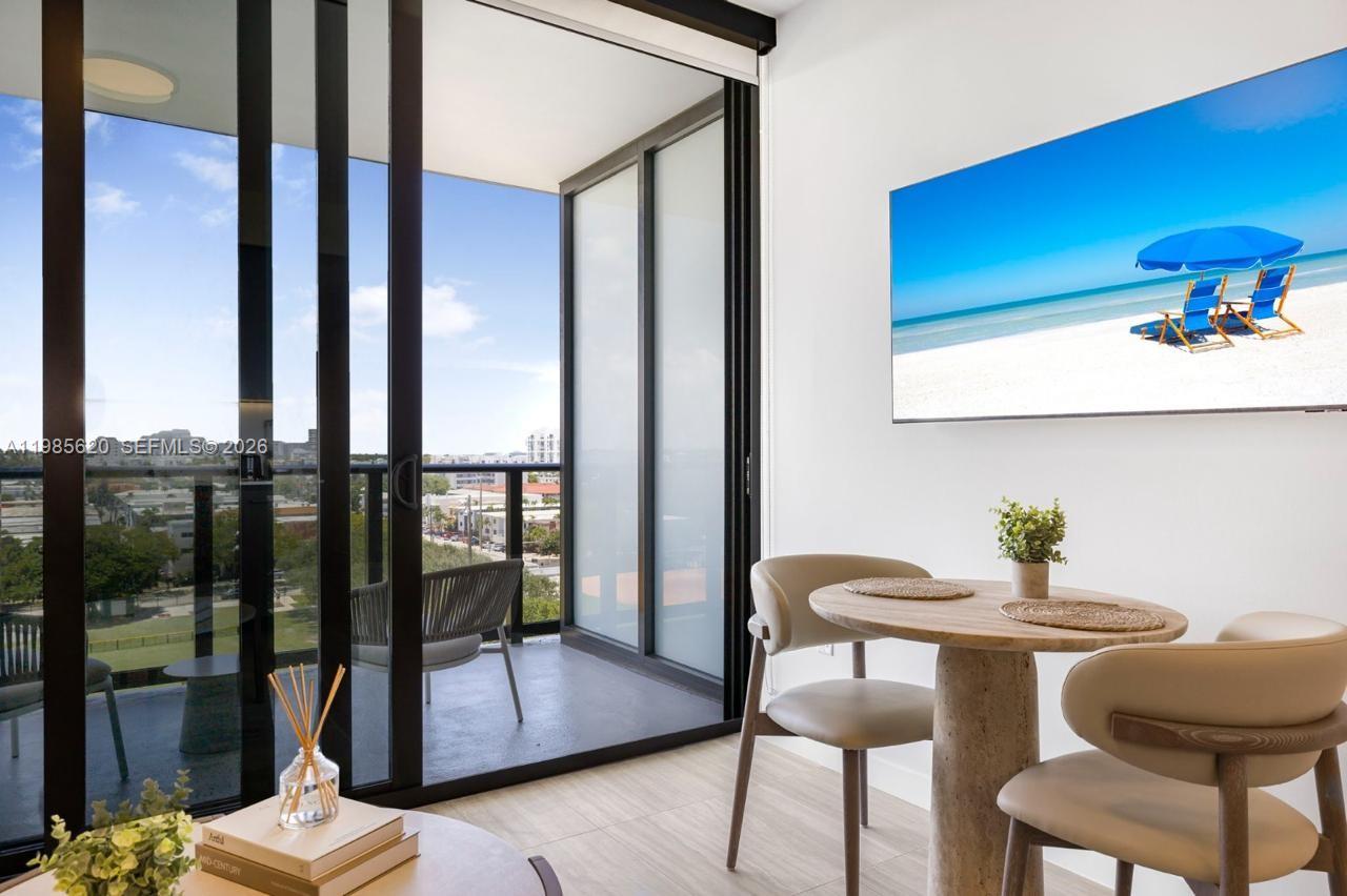 A dining area with a round table and chairs next to a balcony with city views — 580 72nd St # 613, Miami Beach FL 33141, MIAMI BEACH, FL