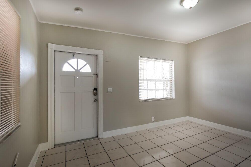 An empty room features light-colored walls, white tile flooring, a front door, and a window — MIAMI, FL