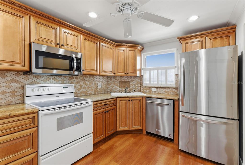 A kitchen features wood cabinets, stainless steel appliances, a white stove, and a tile backsplash — 5980 SHORE BOULEVARD S UNIT 901, GULFPORT, FL