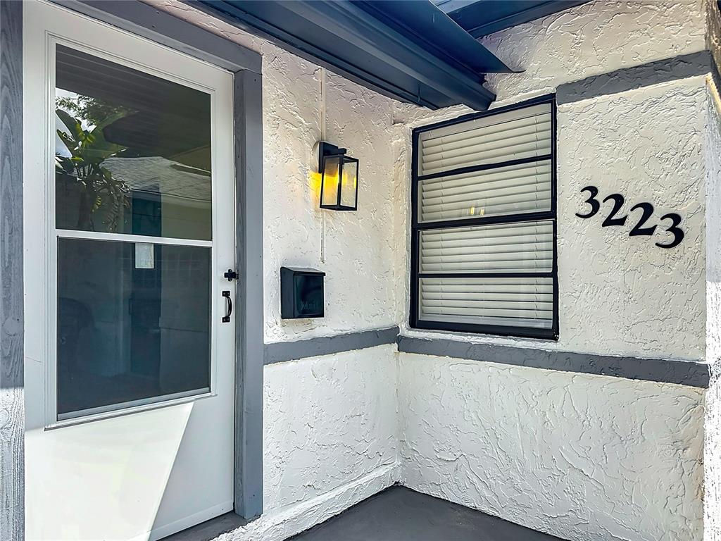 A white stucco exterior wall features a front door, a window, and a mailbox — 3223 N ORANGE AVE, ORLANDO, FL