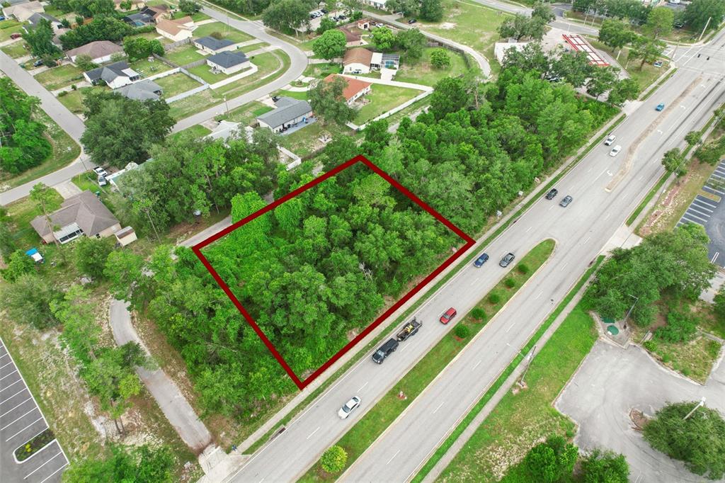 An aerial view shows a rectangular, tree-covered vacant lot outlined in red next to a road — 2841 HOWLAND BOULEVARD, DELTONA, FL