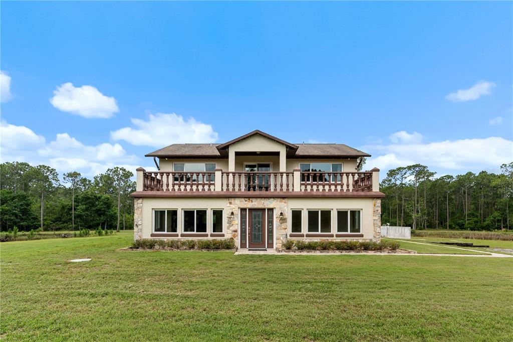 A two-story house with a stone facade, a large upper balcony, and a grassy yard — 204 EL PINO DRIVE, NEW SMYRNA BEACH, FL