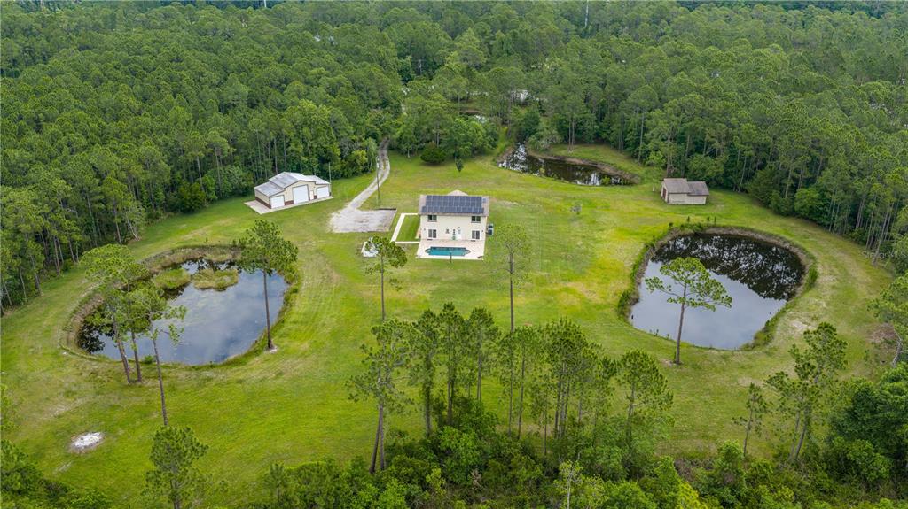 An aerial view shows a house with a pool, two ponds, and a detached garage — 204 EL PINO DRIVE, NEW SMYRNA BEACH, FL