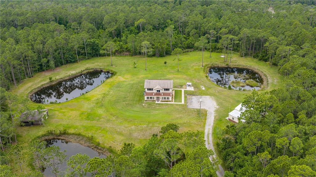 An aerial view shows a house, two ponds, and a small outbuilding surrounded by forest — 204 EL PINO DRIVE, NEW SMYRNA BEACH, FL