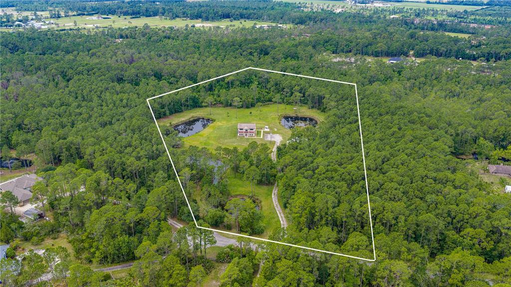 An aerial view shows a house situated on a large, wooded lot with several ponds — 204 EL PINO DRIVE, NEW SMYRNA BEACH, FL